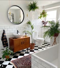 a bathroom with black and white checkered flooring, potted plants and a round mirror