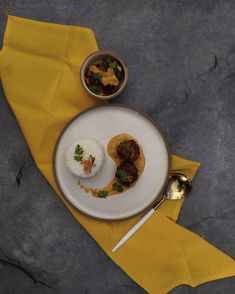 a white plate topped with food on top of a yellow napkin next to a silver spoon