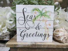 a wooden sign that says seas and greetings on it next to some white flowers