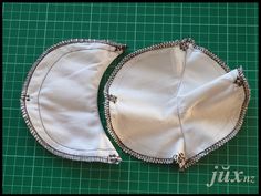 two pieces of white cloth with silver zippers on a green cutting mat next to a pair of scissors