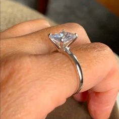 a close up of a person's hand holding a ring with a diamond on it