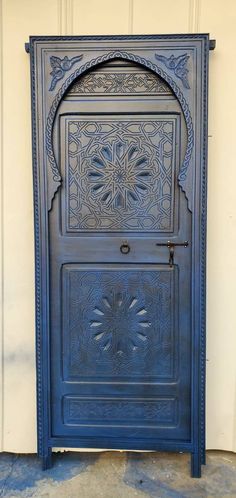 an ornate blue door is shown in front of a white wall and cement flooring