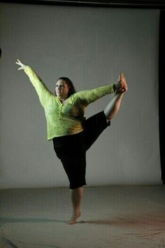 a woman in a green shirt and black pants doing a dance pose