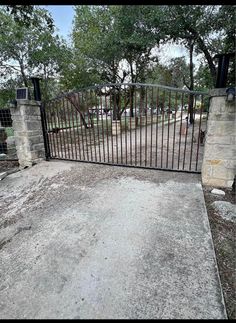 an iron gate is in front of a stone wall and tree - lined driveway area