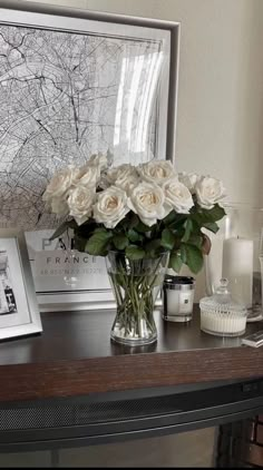 a vase filled with white roses sitting on top of a table next to candles and pictures