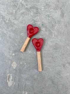 two red heart shaped wooden spoons sitting on top of a cement floor next to each other