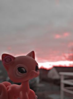 a small toy cat sitting on top of a wooden table next to a window with the sky in the background