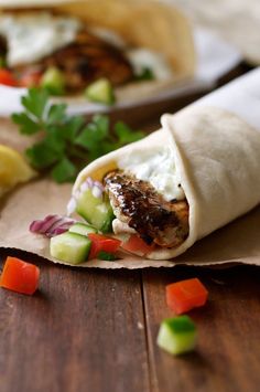 two burritos with meat and veggies on them sitting on a wooden table