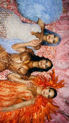 three young women laying on top of a bed covered in orange and blue feathers,