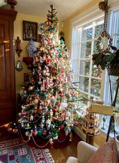 a brightly colored christmas tree is in the corner of a living room with a large window