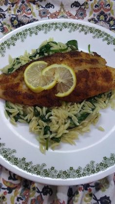 a white plate topped with fish and pasta covered in lemon slices on top of it