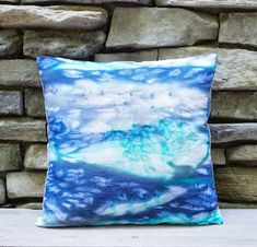 a blue and white pillow sitting on top of a wooden table next to a stone wall