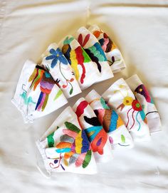 five napkins with colorful designs on them sitting on a white cloth covered tablecloth