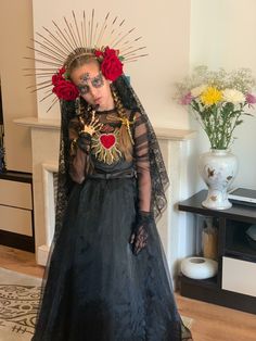 a woman in a black dress with red roses on her head and face, standing next to a fireplace