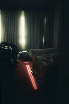 a black and white photo of two beds in a dark room with sunlight coming through the curtains