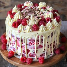 a cake with white frosting and raspberries on a wooden platter,