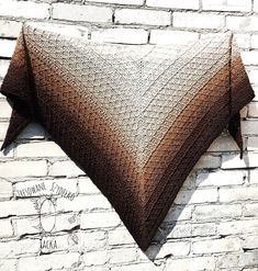 a brown and white knitted shawl hanging on a brick wall