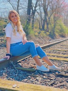 a woman is sitting on the railroad tracks posing for a photo with her legs crossed