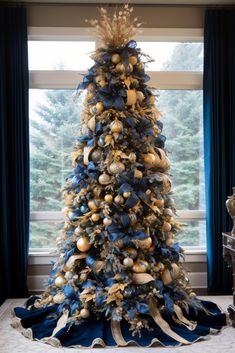 a blue and gold christmas tree in front of a large window with ribbon on it