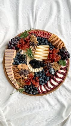 a platter filled with cheese, crackers, grapes and meats on top of a white table cloth