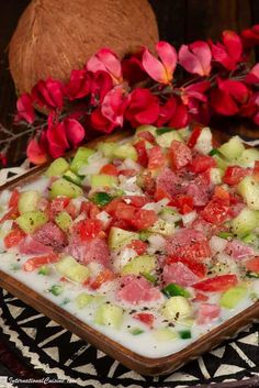 a dish with cucumbers, tomatoes and other vegetables on it next to red flowers