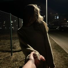 a woman holding onto someone's hand near a fence and street light at night