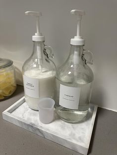 two bottles with soap and lotion sitting on a marble tray next to each other