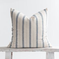 a white and blue striped pillow sitting on top of a wooden bench