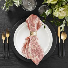 a place setting with black and white plates, silverware, and pink napkins