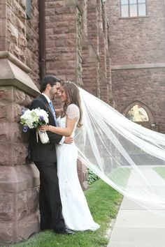 a bride and groom standing next to each other in front of a building with a long veil over their heads