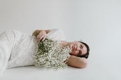 a woman laying on the ground with flowers in her hand and wearing a white dress