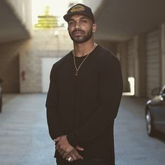 a man standing in an empty parking garage next to his car and wearing a hat