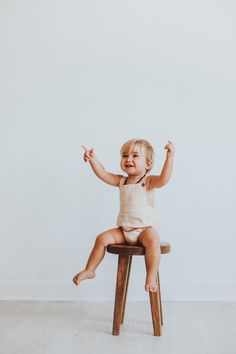 a baby sitting on top of a wooden stool with his arms in the air and smiling