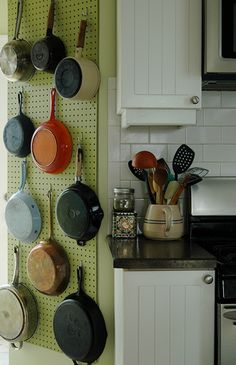 pots and pans are hanging on the pegboard in this kitchen with white cabinets