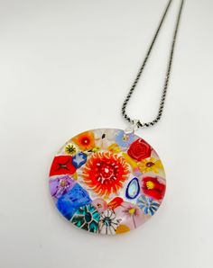 a multicolored glass pendant hangs from a black chain on a white table top