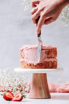 someone is cutting into a strawberry cake with a knife