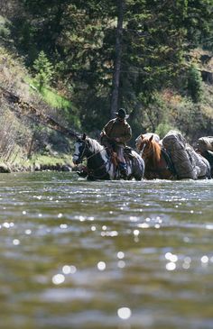 two men on horses crossing a river in front of another man riding one behind them