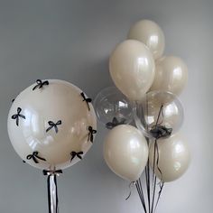 balloons with bows on them are in front of a gray wall and one is white