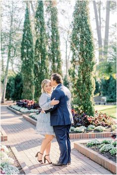 a man and woman standing next to each other on a brick walkway in front of trees