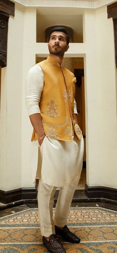 a man standing in front of a doorway wearing a yellow vest and white dress pants