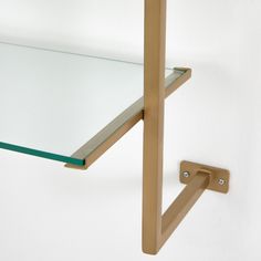 a glass shelf with a metal hook on the side and a white wall behind it