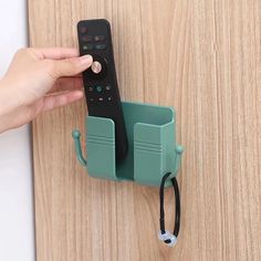 a person is holding a remote control in front of a wall mounted device on a wooden surface