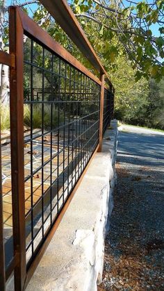 a metal fence is next to a stone wall and tree branches on the side of the road