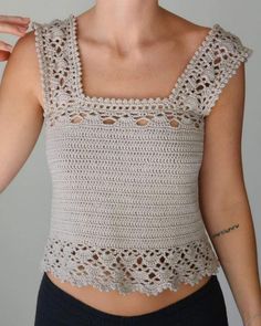 a woman wearing a white crochet top and black pants with her hands on her hips