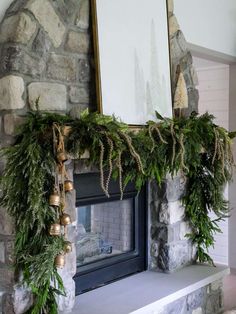 a mantel decorated with greenery and bells in front of a stone fire place