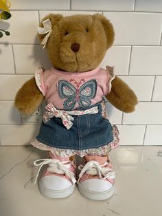 a brown teddy bear wearing a pink shirt and blue jean skirt sitting on top of a counter