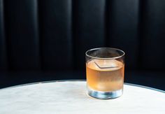 a glass filled with liquid sitting on top of a white table next to a black wall