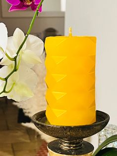 a yellow candle sitting on top of a table next to a vase filled with flowers