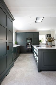 a large kitchen with gray cabinets and white counter tops, along with potted plants