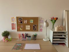 an office desk with various items on it and a cork board attached to the wall